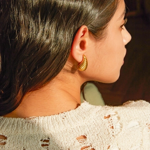 Detail view of gold drop earrings with textured spiral design worn by a female model
