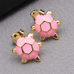 Close-up of pink enamel turtle earrings with gold-plated alloy finish on a grey surface