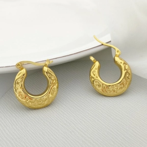 Detail of vintage gold U-shaped hoop earrings with embossed texture and metallic finish