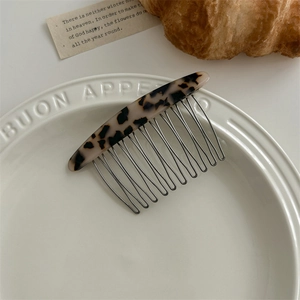 Detail of tortoise shell acetate hair comb with metal teeth on a white ceramic plate