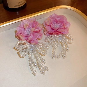 Close-up of pink fabric flower earrings with white pearl bow tassels on a decorative tray