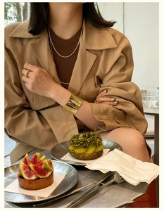 Minimalist wide gold curved open cuff bracelet worn by a model in a luxury cafe setting