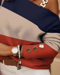 Detalle de blusa con bloques de color, cadena metálica y botones dorados en la manga