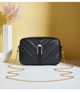Close-up of black textured leather crossbody bag with elegant gold chain and metal lock