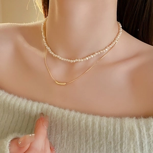 Detail of layered gold snake chain with pearl strand and minimalist curved tube pendant