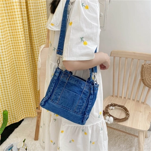 Detail of a dark blue denim crossbody bag with metal buckles and detachable strap