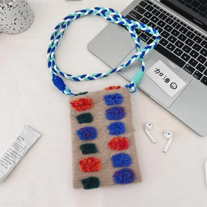 Mini plush crossbody bag with colorful pom-poms and braided strap next to a laptop