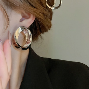 Close-up of a large silver geometric hoop earring worn by a model in a black blazer