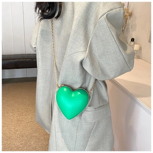 Side view of heart-shaped green crossbody bag with gold chain on model in blazer