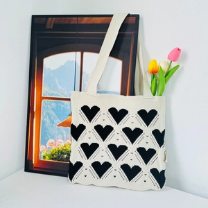 Detail of knitted cream tote bag showing soft texture and black heart pattern with tulips