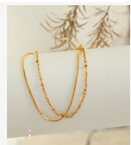 Macro detail of a double-layered gold bracelet featuring a snake chain and bead accents