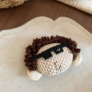 Detailed view of a handmade fabric doll brooch with brown curly hair and sunglasses