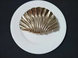 Top view of a gold-plated seashell hair claw clip with metallic texture on white plate