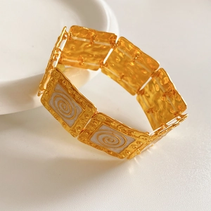 Macro detail of vintage gold square link bracelet with spiral white enamel texture