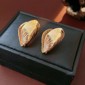 Close-up of golden shell-shaped textured hoop earrings on a black display stand