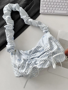 Blue and white striped ruched handbag with white bows and ruffled strap on a desk