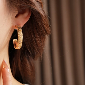 Close-up of gold C-shaped earrings with diamond flower engraving on model's ear
