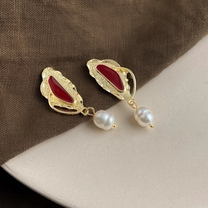 Detail of baroque pearl earrings with golden leaf design and red enamel accents