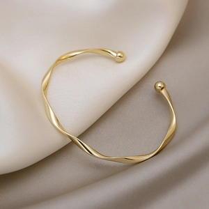 Bracciale rigido dorato a spirale dal design minimalista su un elegante tessuto di seta