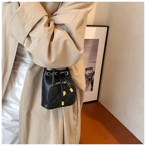 Detail of black quilted bucket bag with golden flower charm on a beige trench coat