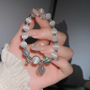 Detail von Katzenaugen-Perlenarmband mit Fu-Anhänger und kleinen Glocken an der Hand