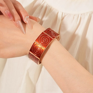 Detail of vintage enamel square bracelet with orange spiral pattern on a female wrist