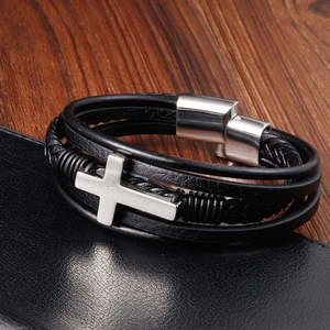 Detail of black multilayer leather bracelet with silver metal cross charm on dark wood