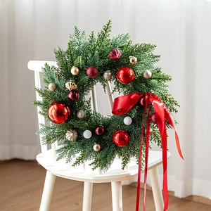 Classic green Christmas wreath with red ornaments and a large bow on a white chair