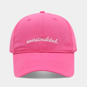 Close-up of white embroidered overstimulated text on pink cotton baseball cap
