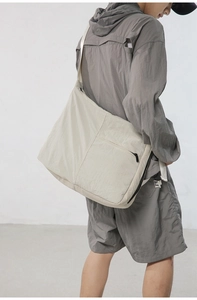 Close-up of a large beige nylon crossbody messenger bag shown in a minimalist lifestyle setting