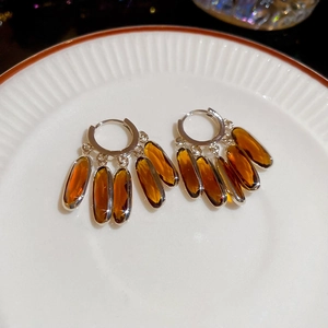 Close-up of vintage silver earrings with amber crystals and five oval tassels in a ceramic dish