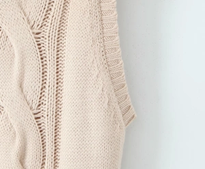 Detailed macro view of beige cable knit texture and ribbed hem finish on the dress
