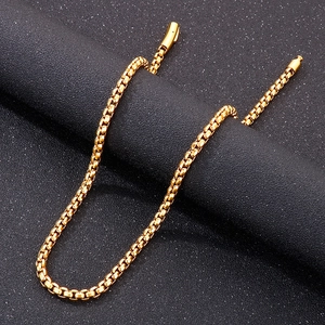 Gros plan d'un collier chaîne box dorée poli sur un support cylindrique texturé foncé