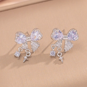 Macro shot of silver bow earrings with heart-shaped zircons and star-shaped pendants