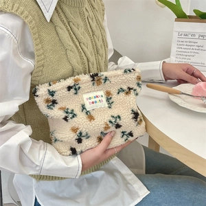 Close-up of floral sherpa fleece cosmetic bag held by a model in a cafe setting