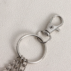 Detail of silver heart-shaped metal carabiner and layered chain hardware for pants