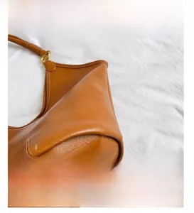 Detailed close-up of brown leather stitching and metallic buckle on the shoulder bag