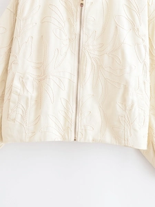 Gros plan de la veste beige avec broderie de feuilles et fermeture éclair en métal