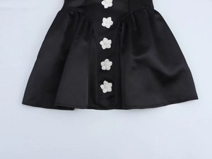 Detail of elegant black satin mini dress featuring five white 3D floral accents and ruffles