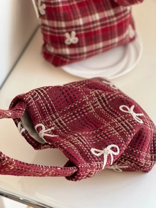 Detail of red plaid wool bag with white embroidered bows on a minimalist pedestal