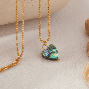 Detail of heart-shaped abalone shell pendant on golden beaded chain with natural texture