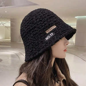 Close-up of black textured knit fisherman hat featuring More and No.17 decorative labels