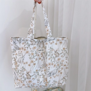 Close-up of cream canvas tote featuring realistic rabbit and floral prints with simple wish label