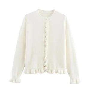 Détail du cardigan blanc avec bords à volants et fermeture à boutons assortis