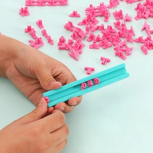 Close-up of pink alphabet stamps being inserted into a blue sliding base for DIY cookies
