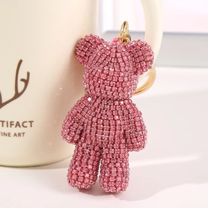 Pink rhinestone cartoon bear keychain with golden clasp hanging on a cream mug