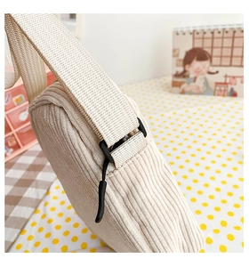 Detail of cream corduroy crossbody bag showing wide fabric strap and plastic buckle