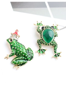 Detail of two cartoon frog brooches featuring green enamel and a large drop gemstone