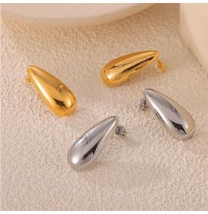 Close-up of teardrop stud earrings in gold and silver finish on a textured background