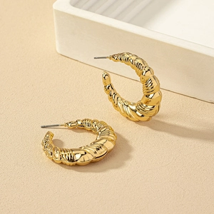 Detailed view of chunky gold-plated C-shaped twisted hoops with textured wave patterns